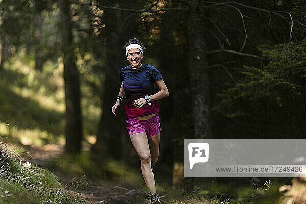 Glückliche junge Sportlerin beim Laufen im Wald