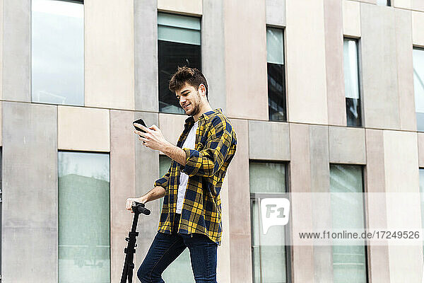 Smiling man using mobile phone while standing in front of building