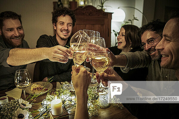 Lächelnde Freunde stoßen bei einer Feier zu Hause mit Weingläsern an