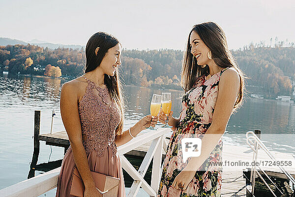 Schöne Frauen mit Trinkgläsern stehen auf einem Steg über einem See
