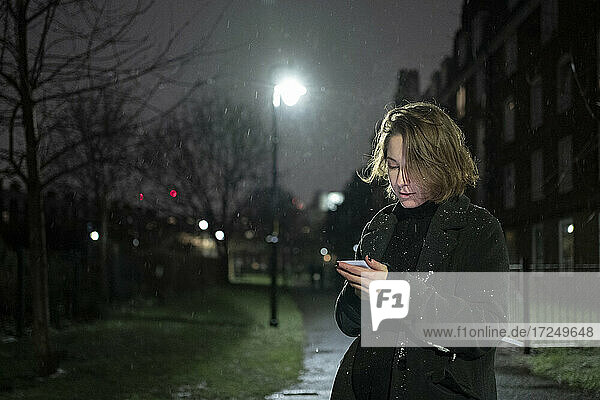 Frau benutzt Mobiltelefon  während sie nachts auf der Straße steht