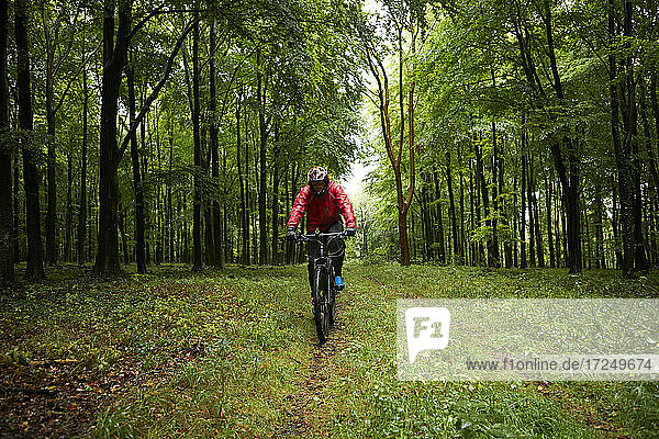 Male athlete wearing protective sportswear riding bicycle on forest path
