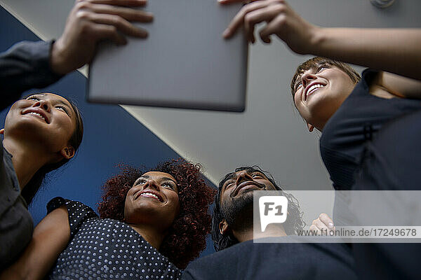 Lächelnde internationale männliche und weibliche Fachkräfte  die wegschauen und ein digitales Tablet im Büro halten