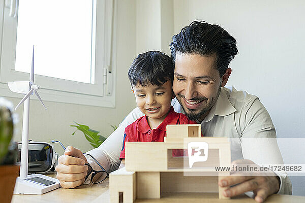 Männlicher Architekt und Sohn lächelnd bei der Betrachtung eines Hausmodells