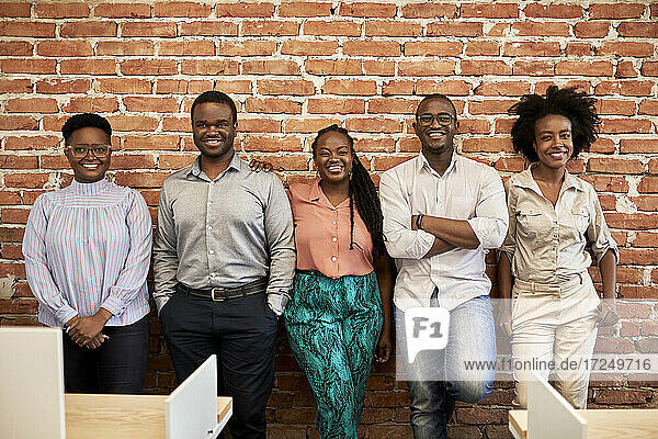 Smiling male and female professionals standing together in front of brick wall in coworking office