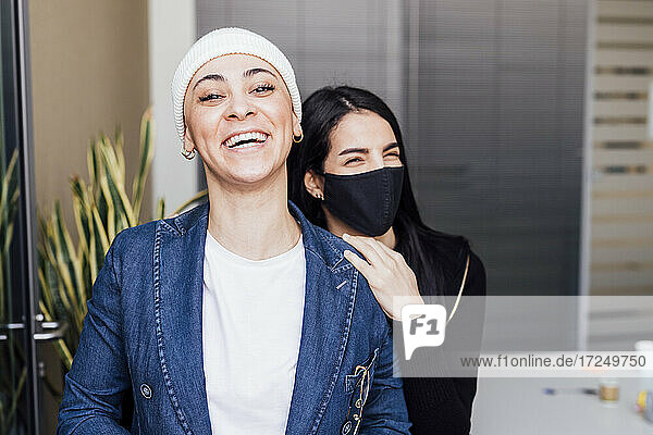 Glückliche Geschäftsfrau und Kollegin mit Gesichtsschutzmaske im Büro