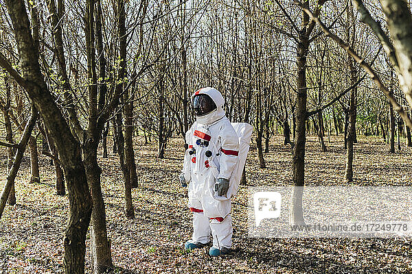 Astronaut wearing space suit and helmet looking away in forest