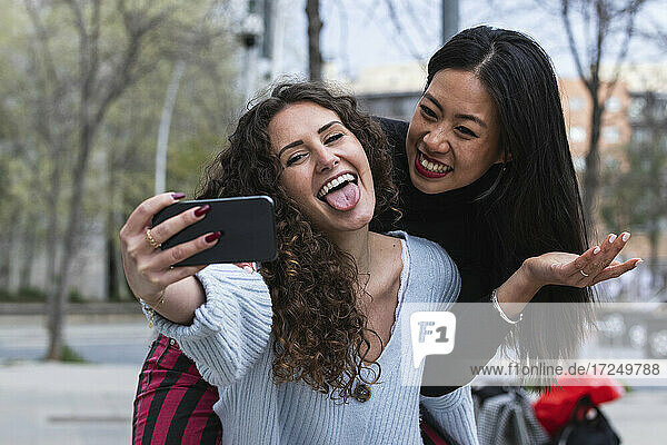Verspielte Frau  die einen Freund huckepack nimmt  während sie ein Selfie mit dem Handy macht