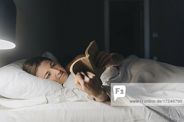 Woman reading book while lying on bed in hotel room