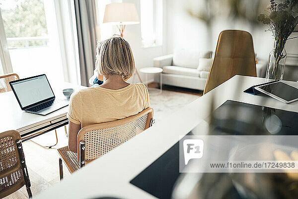 Kurzhaarige Geschäftsfrau schaut im Wohnzimmer auf ihren Laptop