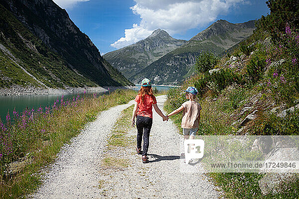 Schwestern halten sich an den Händen  während sie an einem sonnigen Tag im Zillertal  Österreich  spazieren gehen