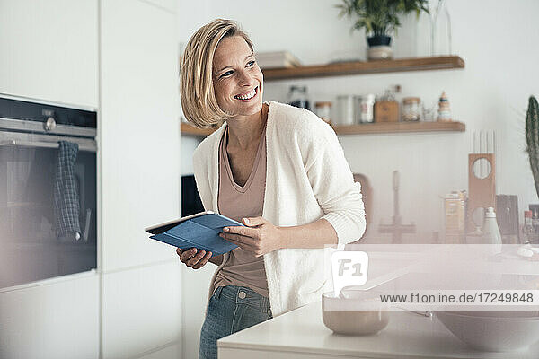 Lächelnde Frau  die wegschaut  während sie sich zu Hause auf die Küchentheke stützt