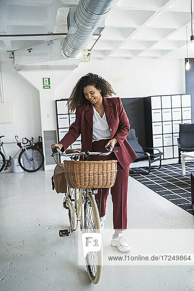 Smiling female professional wheeling bicycle in coworking office