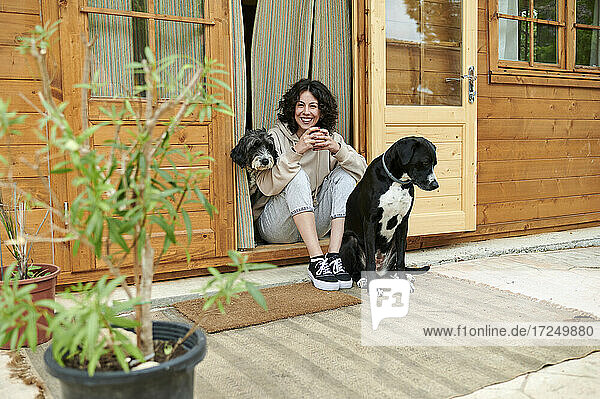 Glückliche Frau sitzt inmitten von Hunden vor der Tür