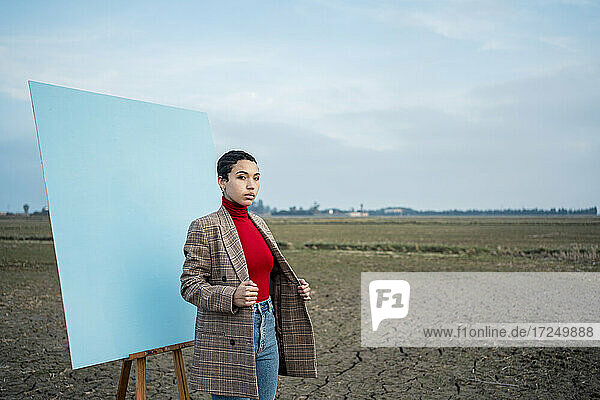 Frau in Jacke vor einem Bild auf einem Feld stehend