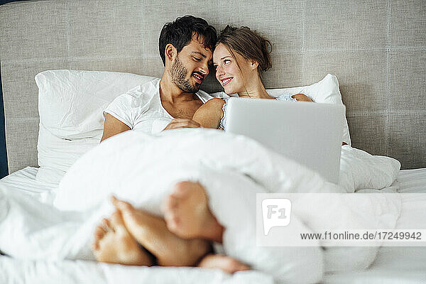 Lächelndes Paar  das sich auf dem Bett sitzend gegenseitig ansieht