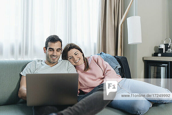 Woman leaning on man using laptop while sitting on sofa in hotel