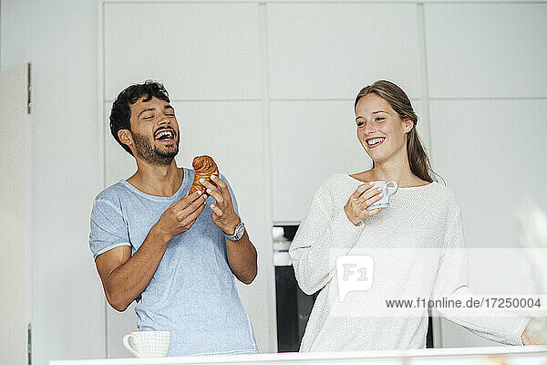 Glücklicher Mann mit Croissant bei seiner Freundin in der Küche zu Hause