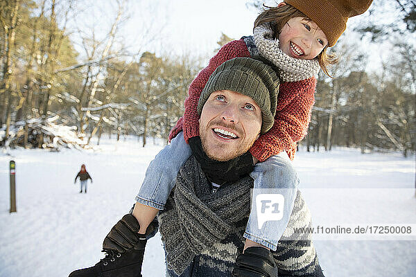 Father looking up while carrying son on shoulder during winter