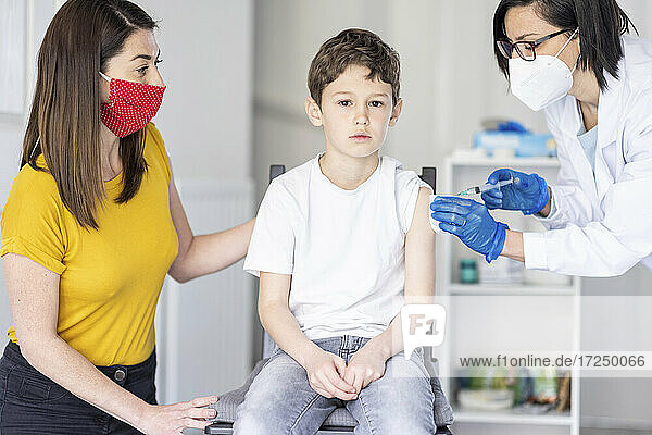 Mutter betrachtet ihren Sohn  der von einer Ärztin in einer Klinik während der Pandemie gegen COVID geimpft wird
