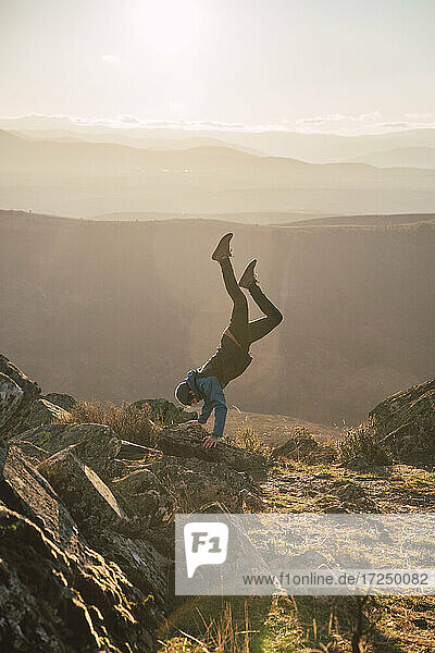 Male sportsperson exercising while doing handstand on mountain