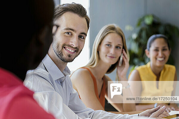 Lächelnder Geschäftsmann neben weiblichen Kollegen im Büro sitzend