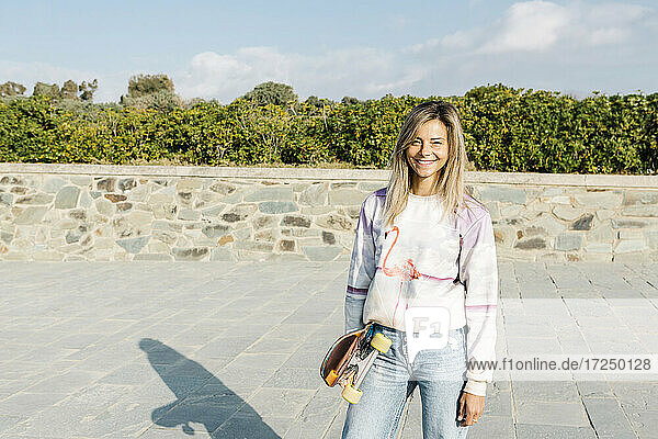 Lächelnde Frau mit Skateboard im Park an einem sonnigen Tag