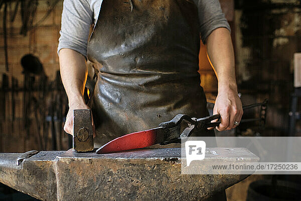 Schmied macht Messer aus Metall auf Amboss in Schmiede