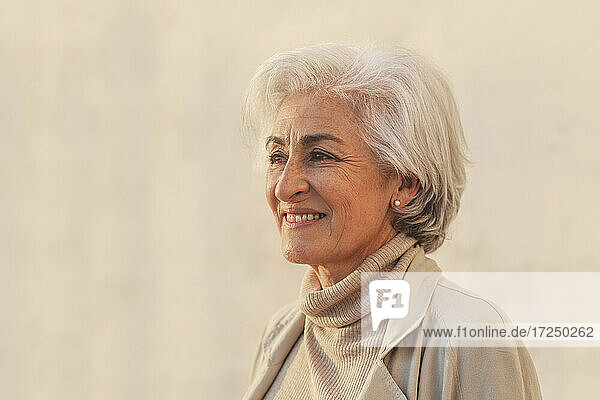 Smiling mature woman contemplating by beige wall