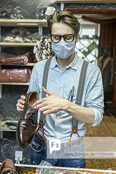 Männliche Fachkraft mit Schutzmaske  die einen Schuh in einem Geschäft während COVID-19 hält