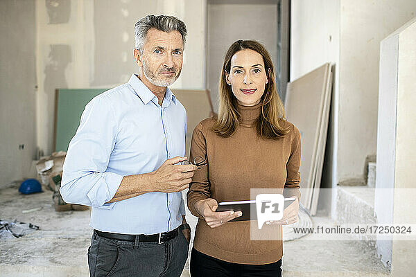 Weiblicher Kollege mit digitalem Tablet neben einem gut aussehenden männlichen Architekten auf der Baustelle