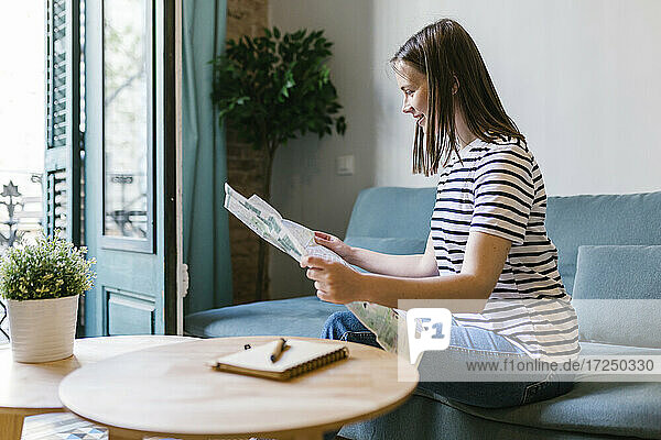Lächelnde junge Frau liest Zeitung  während sie auf dem Sofa im Ferienhaus sitzt