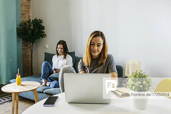 Young woman using laptop while sitting at table in living room