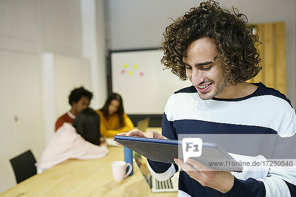 Smiling creative businessman holding digital tablet in office