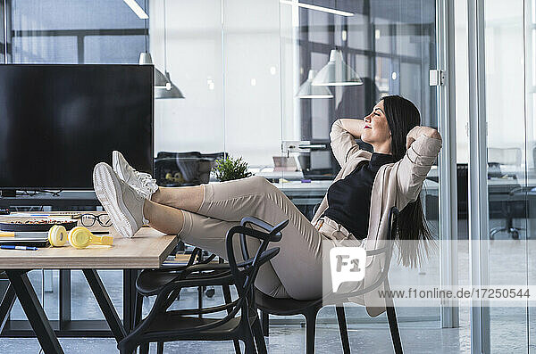 Geschäftsfrau mit Händen hinter dem Kopf entspannt am heißen Schreibtisch im Büro