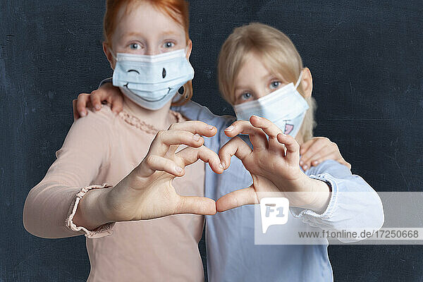 Sisters machen Herzform mit Händen tragen Gesichtsmaske gegen schwarzen Hintergrund