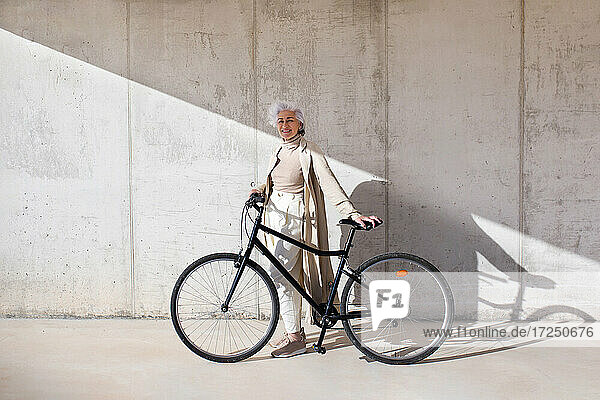Lächelnde Frau mit Fahrrad auf dem Fußweg stehend
