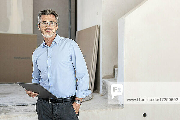 Male architect with hand in pocket holding digital tablet at site