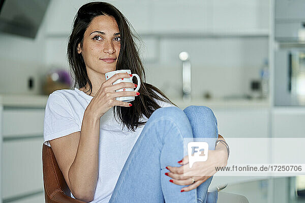 Lächelnde Frau sitzt mit Kaffeetasse und schaut weg