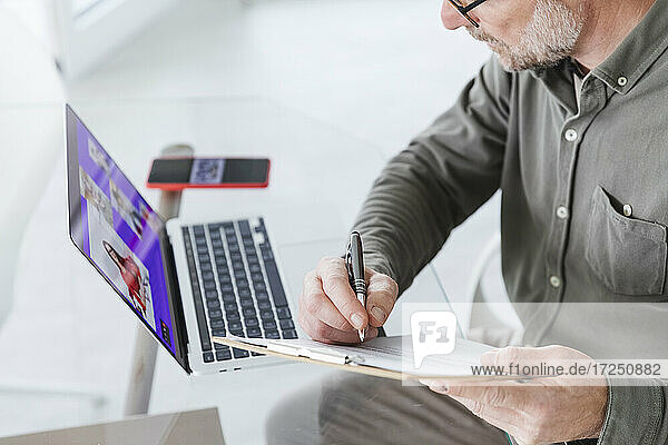 Älterer Geschäftsmann arbeitet während einer Videokonferenz über einen Laptop im Büro