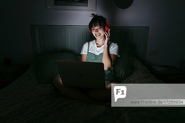 Lächelnde Frau mit Kopfhörern  die zu Hause einen Laptop benutzt