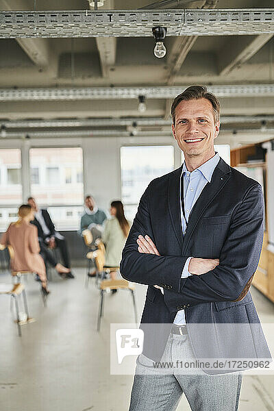 Reifer männlicher Unternehmer mit Kollegen im Hintergrund im Büro stehend