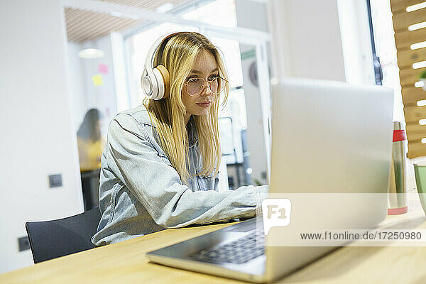Blonde Geschäftsfrau mit Laptop und Kopfhörern im Büro