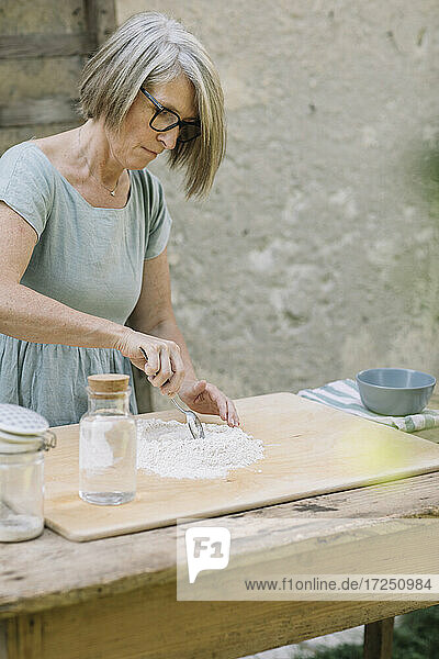 Reife Frau beim Mischen von Mehl und bei der Zubereitung von Teig im Vorgarten oder Hinterhof