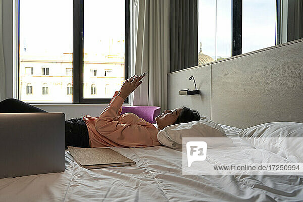 Weibliche Berufstätige  die mit ihrem Smartphone Textnachrichten verschickt  während sie auf dem Bett im Hotel liegt