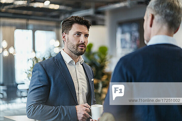 Mid adult businessman talking with male colleague in office cafe