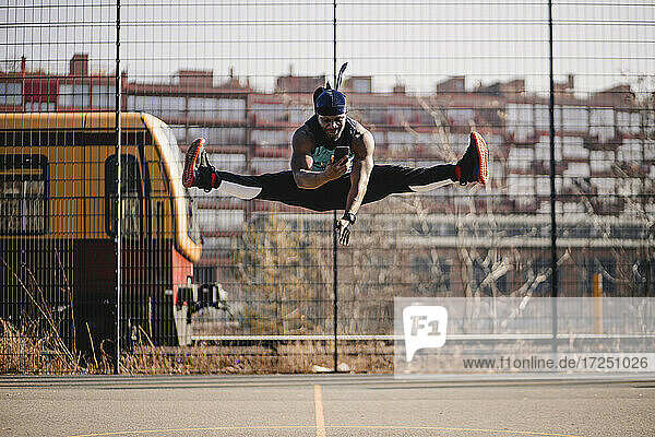 Afrikanischer Mann benutzt Mobiltelefon beim Springen auf dem Sportplatz