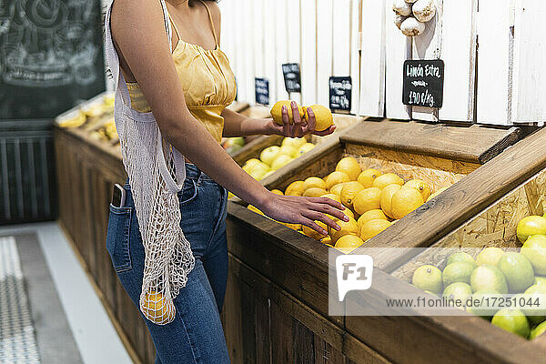 Frau mit Netzbeutel beim Kauf von Zitronen im Supermarkt