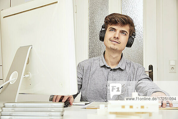 Männlicher Architekt schaut weg  während er im Büro über Kopfhörer Musik hört