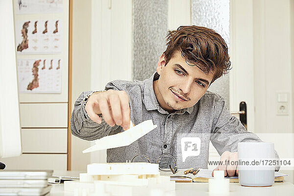 Männlicher Architekt arrangiert Modell  während er im Büro sitzt